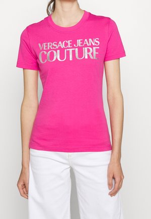 Fuchsiové bavlněné tričko s nápisem "VERSACE JEANS COUTURE" ve stříbrném kovovém provedení. Klasický kulatý výstřih a krátké rukávy.