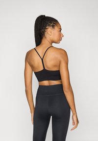 Μαύρο αθλητικό μπουστάκι με λεπτούς, σταυρωτούς ιμάντες στην πλάτη, αδιάκοπη σχεδίαση και συνδυασμένο με μαύρο κολάν ψηλόμεσο. Ομαλή υφή.