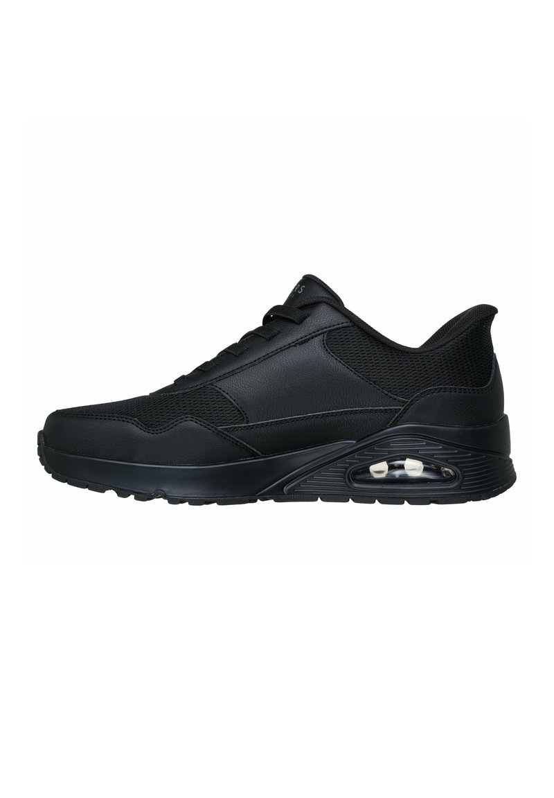 Zapato deportivo negro hecho de cuero sintético y malla, con punta redondeada, cordones en la parte frontal y amortiguación de aire visible en la suela.