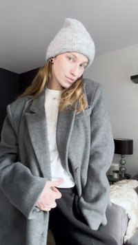 Szürke gyapjú kabát nagy hajtókákkal, gombbal díszített és túlméretezett ujjakkal. Fehér felsőre viselve, szürke kötött sapkával párosítva.