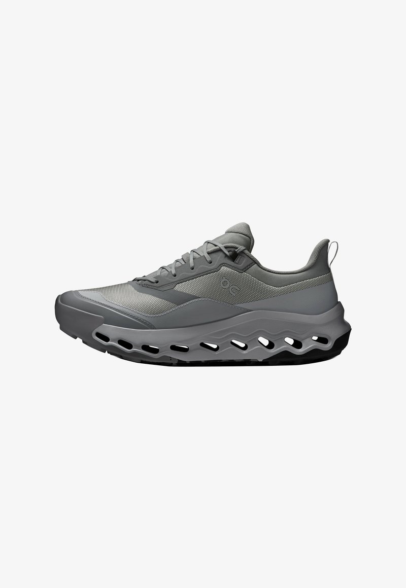 Chaussure de sport grise avec une tige en mesh, une semelle coussinée et un design ondulé distinctif. Comprend des lacets et une languette au talon.
