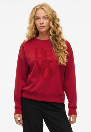 Rotes Sweatshirt in lockerer Passform, mit einem großen "BE YOU"-Text in einem dunkleren Farbton. Entworfen mit einem runden Halsausschnitt und gerippten Bündchen.