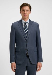 Donkerblauwe colbert met een gestructureerde afwerking, enkelzijdig ontwerp, twee voorzakken en een gelapiseerde revers. Gecombineerd met een lichtblauw overhemd en een gestreepte stropdas.
