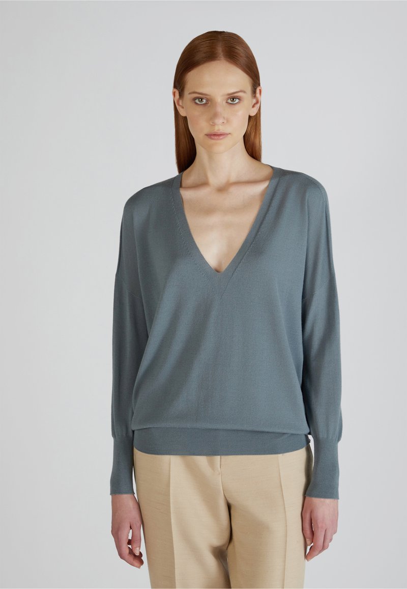 Helles blaues V-Ausschnitt-Pullover mit langen Ärmeln und geripptem Saum; aus einem weichen Strickmaterial gefertigt, kombiniert mit beigen Hosen für den Kontrast.