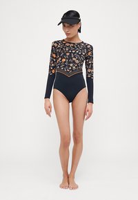 Maillot de bain à manches longues avec un haut à motifs floraux dans des couleurs sombres et un bas uni. Il présente un col montant et est fabriqué en tissu de bain.