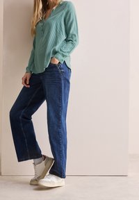 Lysegrøn, langærmet skjorte med knaplukning og ribbet tekstur, parret med blå lige ben jeans og hvide sneakers.