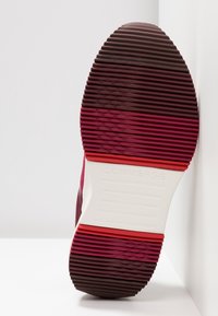 Podeszwa trampka Converse w kolorze bordowym z teksturowanymi żłobieniami, z gradientowym przejściem kolorów do czerwono-pomarańczowego przy podstawie pięty.