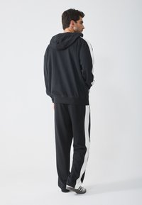 Zwarte hoodie met witte zijstrepen, relaxed fit, vervaardigd uit een katoenmengsel. Gecombineerd met bijpassende zwarte broek met witte accentstrepen.