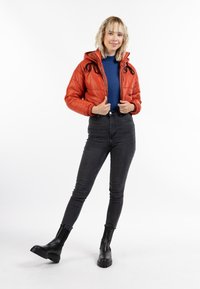 Giacca a vento rossa con cappuccio, lacci neri, top blu, jeans neri a vita alta e stivaletti neri con suola spessa.