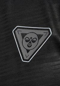 Schwarzer Stoff mit einem dreieckigen Aufnäher, der ein stilisiertes Gesichtslogo zeigt, weiß umrandet und zentral positioniert. Die Textur wirkt glatt mit dezenten Mustern.