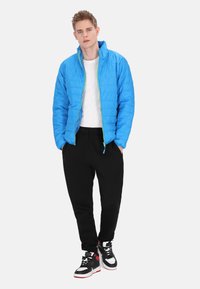 Blå pufferjakke med grønner lynlås, hvid t-shirt, sorte sweatpants og sort-hvide høj-top sneakers. Glat tekstur.