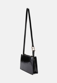 Čierna kožená crossbody taška so štíhlym obdlžníkovým tvarom. Obsahuje dlhý popruh a jemný lesklý povrch. Kompaktný a minimalistický dizajn.