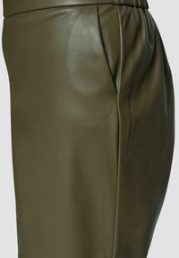 Olijfgroene leren rok met een gladde textuur. Beschikt over een elastische tailleband en subtiele plooien aan de zijkant voor extra ontwerpelement.