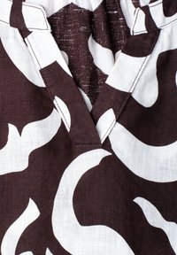 Gros plan sur un tissu marron et blanc avec des tourbillons abstraits et une couture de col pliée.