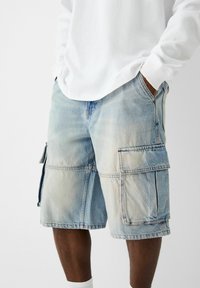 Světle modré denimové cargo šortky s několika kapsami, volným střihem a vybledlým povrchem. Spárovány s bílou košilí s dlouhým rukávem.