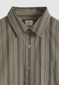 Cămașă kaki cu nasturi, cu guleraș și dungi verticale gri închis, având un buzunar la piept, care afișează eticheta brandului Levi’s în interiorul gulerului.