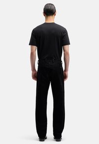 Czarna koszulka i czarne spodnie sztruksowe o prostym kroju. Tkanina ma miękką fakturę, z widocznymi przeszyciami i klasycznym fasonem.