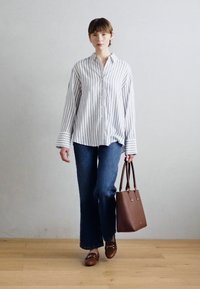 Chemise à rayures, jeans évasés bleu marine, sac à main marron et chaussures assorties. Texture lisse, coupe soignée et détails subtils.