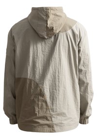 Giacca leggera beige con cappuccio, caratterizzata da una superficie texturizzata, un design curvo che combina sezioni beige più chiare e più scure, e dettagli gialli.