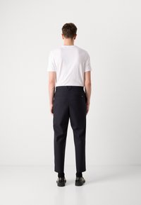 Navy trousers with a straight-leg cut, belt loops, and two rear pockets. Paired with a plain white t-shirt and black shoes.