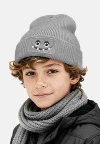 Gray knitted beanie featuring a cartoon monster face with large eyes and fangs. Accompanied by a thick, gray knitted scarf.