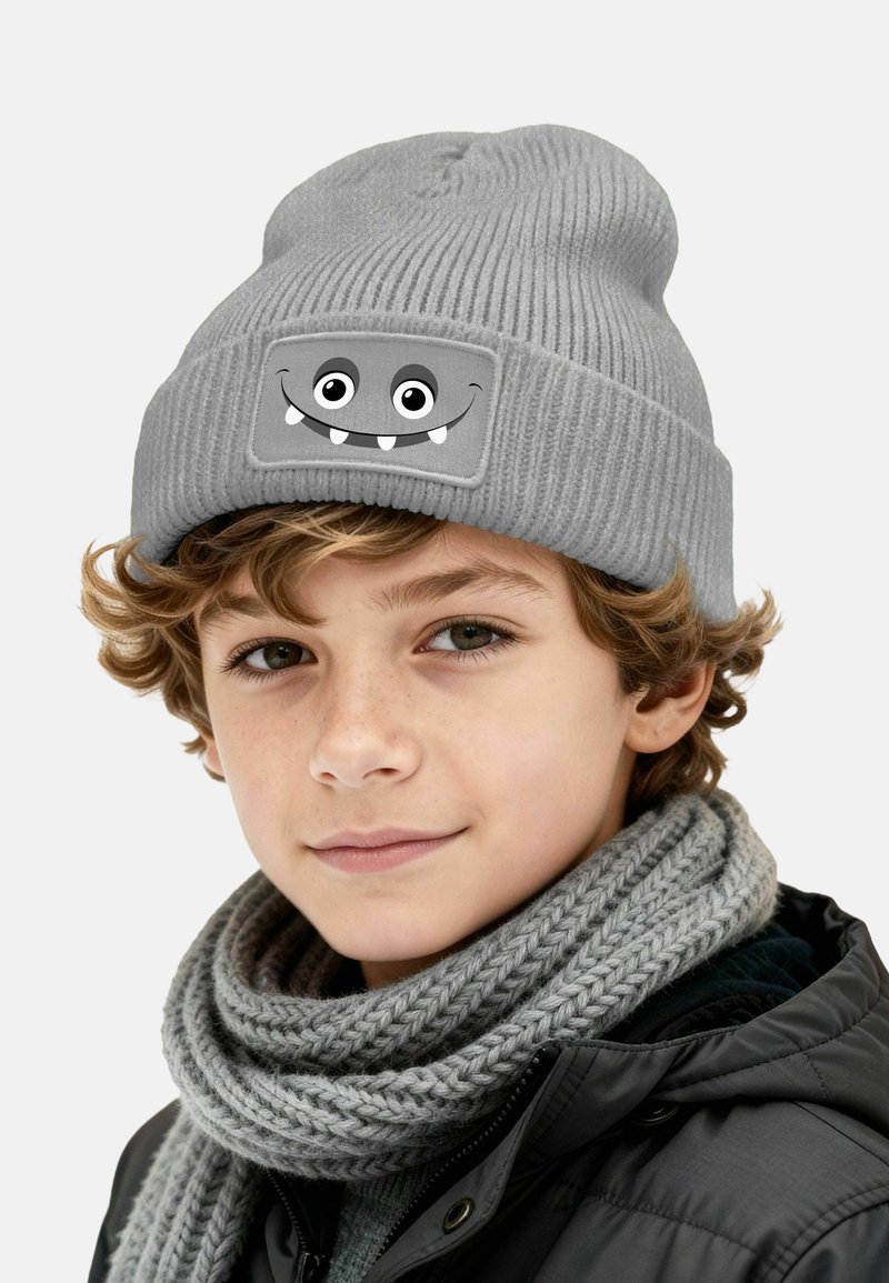 Gray knitted beanie featuring a cartoon monster face with large eyes and fangs. Accompanied by a thick, gray knitted scarf.