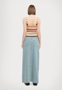 Gestreifter Cropped-Top mit verstellbaren Trägern, kombiniert mit einem langen, hellblauen Jeansrock mit aufgesetzten Taschen und geradem Schnitt.