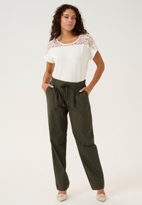 Top bianco con dettagli in pizzo e maniche corte abbinato a pantaloni verde oliva, larghi, con vita elastica e cordoncino.
