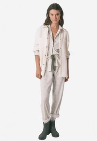 Lysegråt pyjamasæt med små mønstre, kombineret med en hvid skjorte med knapper. Mørkegrønne gummistøvler. Blødt stof, afslappet pasform.