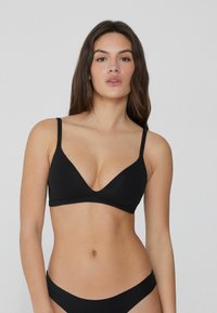 Zwarte driehoek bralette gemaakt van zachte stof, met dunne verstelbare bandjes en een diepe V-halslijn, gecombineerd met bijpassende zwarte bikini broekjes.