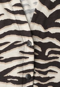 Gros plan sur un tissu rayé zèbre noir et beige avec deux boutons noirs cousus sur un col en V.