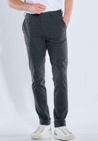 Graue, schmal zulaufende Hose aus weichem Stoff, mit seitlichen Taschen, einem vorderen Knopf und umgeschlagenen Säumen, kombiniert mit weißen Sneakern.