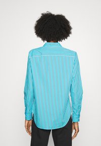 Skjorta med knappar i ljusblått med smala vita vertikala ränder; långa ärmar; tyget har en slät textur; rundad fåll bak.