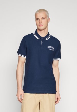 Polo náutico con cuello y puños de manga a rayas blancas. Presenta un logo bordado de "TOMMY JEANS". Tejido de textura suave, corte clásico.