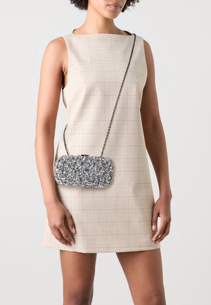 Silberne Perlen-Clutch mit rechteckiger Form, Kettenriemen und strukturiertem Oberflächen. Getragen mit einem beigen, karierten ärmellosen Kleid.