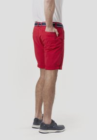 Rdeče bombažne kratke hlače z zavihanimi robovi, elastičnim pasom z mornarsko modro in belo črtasto podrobnostjo ter zadnjim žepom.