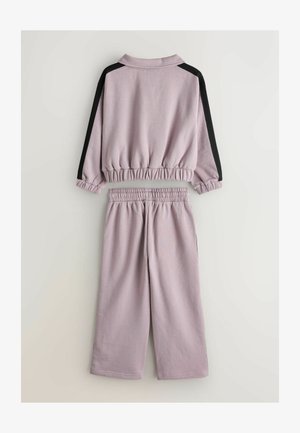 Lila kratka majica z elastiko na manšetah in pasu, v kombinaciji z ujemajočimi širokimi hlačami s črnimi stranskimi poudarki. Mehka tkanina.