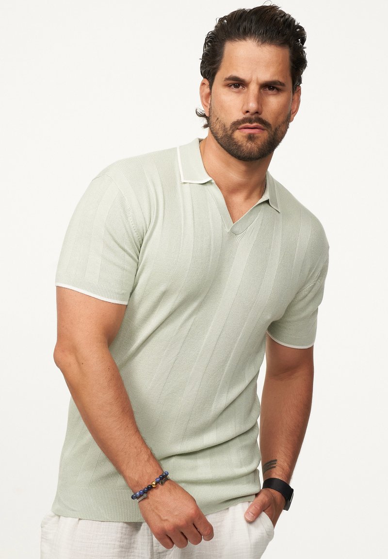 Hellgrünes Polohemd mit kurzen Ärmeln und V-Ausschnitt, ausgestattet mit vertikalen Streifen und weißen Akzenten am Kragen und den Ärmeln.