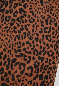 Tkanina s leopardím potiskem v hnědé barvě s černými skvrnami, která má hladký povrch a viditelné detaily prošívání.