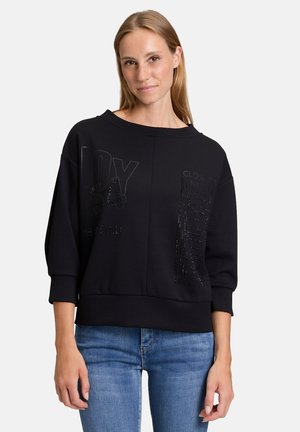 Black sweatshirt with a loose fit, wide neckline, and three-quarter sleeves. Features embossed text and shiny accents on the front.