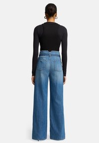 Body nero a coste e jeans in denim azzurro chiaro a gamba larga con tasche posteriori e texture sbiadita, mostrati da dietro.