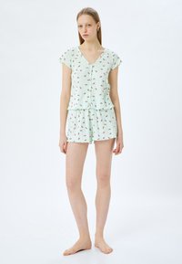 Hellgrünes Pyjama-Set mit kurzen Ärmeln und Shorts, das über eine geknöpfte Vorderseite und ein Wassermelonenkerne-Muster verfügt. Aus weichem, leichtem Stoff.