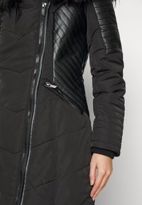 Abrigo de invierno negro con tejido acolchado y detalles de cuero sintético, cierre de cremallera y puños acanalados.