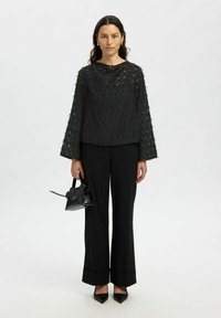 Top lungo a maniche lunghe nera con scollatura rotonda, abbinato a pantaloni neri a gamba larga e una piccola borsa nera.