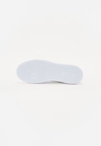 Hvit fotsåle med strukturert mønster, som har et rundt design og vinklede spor for grep. Jevnt materiale generelt.