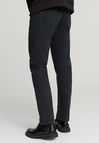 Jeans di denim neri con una vestibilità slim, dotati di due tasche posteriori e un finishing pulito. Accoppiati con scarpe nere lucide.