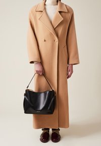 Camelwollmantel mit doppelter Knopfleiste, oversized Revers und Seitentaschen. Schwarze Lederhandtasche mit glatter Oberfläche und Schulterriemen.