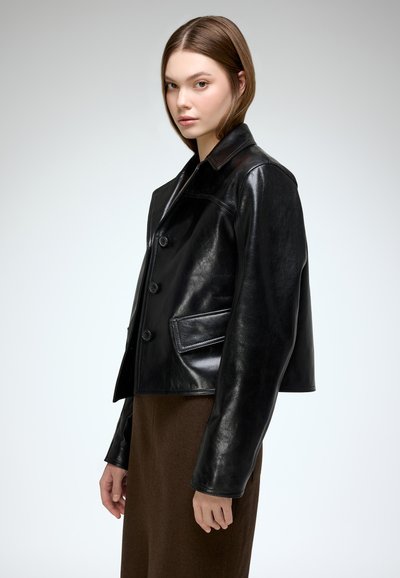 Black leather cropped jacket with a button closure, pointed collar, and side pockets. Smooth texture and tailored fit.