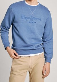 Sudadera de cuello redondo azul, confeccionada en una tela suave, que presenta el texto bordado "Pepe Jeans London" en el pecho y puños y dobladillo acanalados.