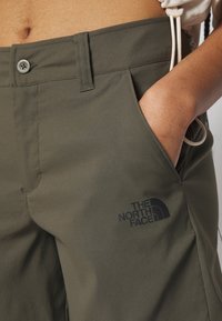 Olivgrüne Hose aus strapazierfähigem Stoff, mit Knopfverschluss, Seitentaschen und dem North Face-Logo auf der linken Tasche.